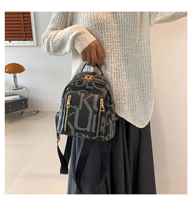 Detailed view of mini black backpack with KUB patterns and golden hardware held by hand