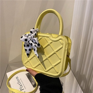Detail of yellow quilted shoulder bag with diamond pattern and polka dot scarf decoration