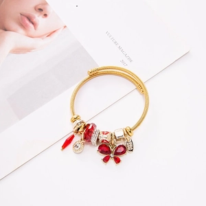 Close-up of gold wire bracelet with red butterfly and crystal charms on magazine background