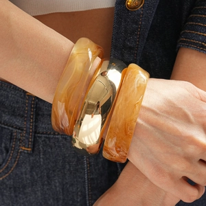 Close-up of amber resin bangles and gold mirror metal cuff worn on denim background