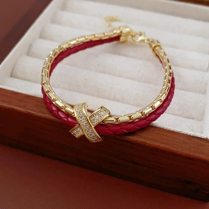 Detail of red braided bracelet with gold plated zircon X-shaped charm in velvet jewelry box