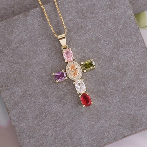 Macro detail of 18K gold cross pendant with colorful oval zircons on grey stone