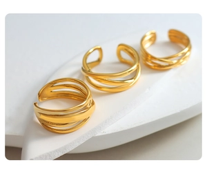 Detailed view of three stackable gold criss-cross rings on a minimalist white stone surface