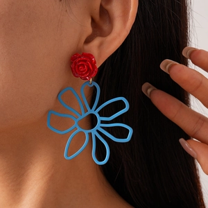 Détail de grandes boucles d'oreilles fleurs bleues évidées avec clou rose rouge sur modèle