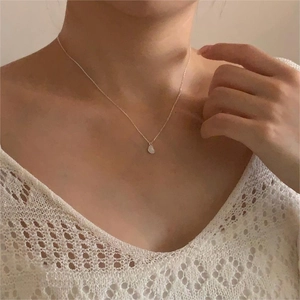 Close-up of a silver necklace featuring a milky white bean pendant on a female model