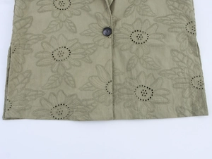 Close-up of olive green floral embroidery and black button detail on blazer fabric