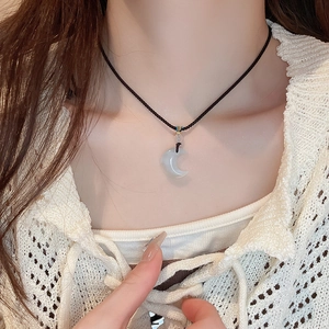 Close-up of a moon-shaped jade-like pendant on a black braided cord necklace for women
