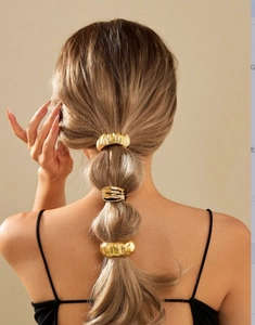 Detailed view of three gold metallic ponytail cuffs on a model styled in a layered hairstyle