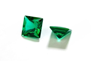Macro view of two princess cut emerald green lab-grown gemstones showing facets and depth