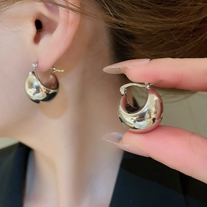 Macro detail of chunky silver drop hoop earrings featuring a high-polish mirror finish