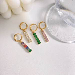 Golden drop earrings with colorful zircon pendants and geometric accents on textured background