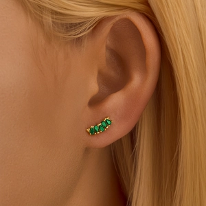 Close-up of gold diamond-studded flower earring with green zircons worn on model ear