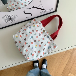 Borsa in tela a fiori con manici rossi e motivi di orsi su un tavolo bianco