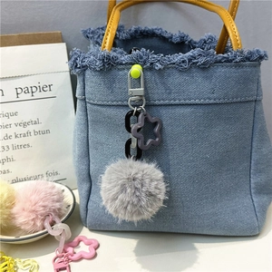 Detail of soft grey plush ball pendant with purple star clip hanging on a denim handbag