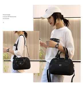 Close-up of black nylon handbag showing round metallic logo and adjustable crossbody strap