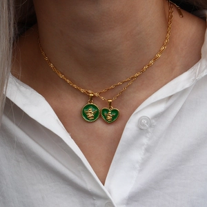 Gold rope chain necklace with green enamel heart and angel pendants worn on a white shirt