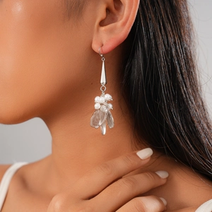 Close-up of silver drop earrings with white pearls and leaf-shaped metal tassel details
