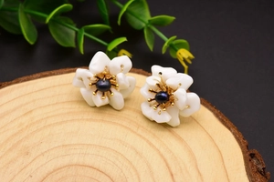 Macro shot of pearl flower earrings on a textured wood background with green leaves