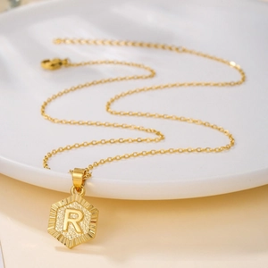 Detail of a gold hexagonal pendant featuring a 3D letter R on a fine cross chain