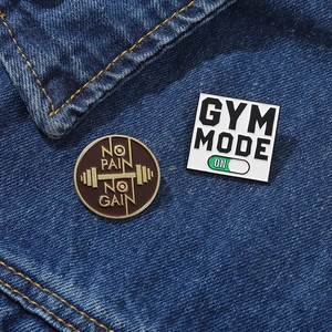 Detail of round No Pain No Gain and square Gym Mode enamel pins on denim jacket