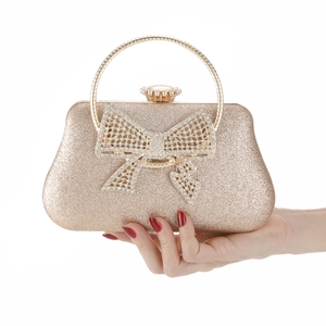 Champagne gold evening clutch with crystal-encrusted bow and metal handle held in hand