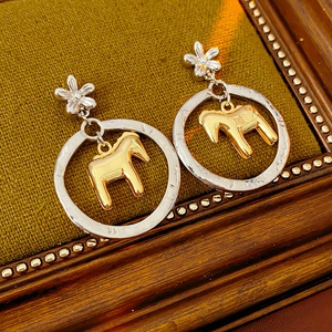 Detail shot of silver flower stud earrings with a gold pony inside a textured ring