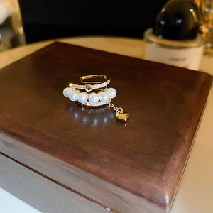 Detailed close-up of gold plated ear cuff with white pearls and zircon heart tassel
