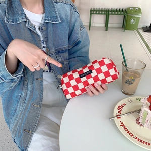 Detail shot of a red and white checkered corduroy pencil case held by a model with cafe props