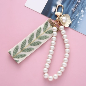 Elegant pearl keychain with leaf embroidery ribbon and gold shell charm on pink background