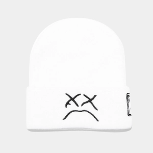Detailed view of white knit beanie featuring black sad face embroidery and side woven label