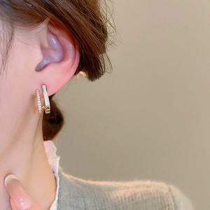 Detail view of double-layered C-shape gold earrings with zircons on a female model
