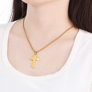 Close-up of a polished gold cross pendant necklace on a model wearing white