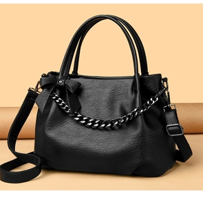 Close-up of black leather texture with metallic chain and bow detail on the tote bag