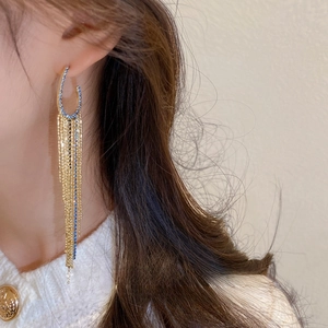 Close-up of long gold tassel earrings with emerald accents and sparkling leaf leaf details