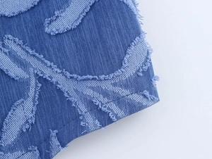 Macro shot of blue denim jacquard fabric with frayed edges and embroidered texture