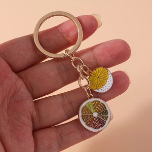 Close-up of golden keychain with enamel lemon and orange fruit slice charms