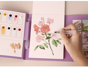 Detailed close-up of a portable watercolor set showing a hand painting a pink rose on paper