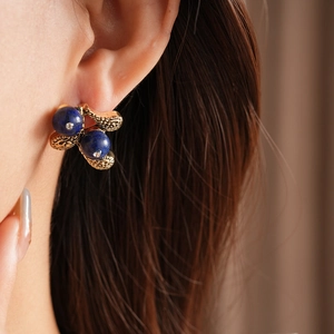 Close-up of vintage golden floral earrings with blue gemstone beads on model ear