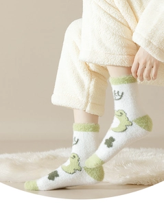 Close-up of white plush socks featuring green frog and clover patterns for winter warmth