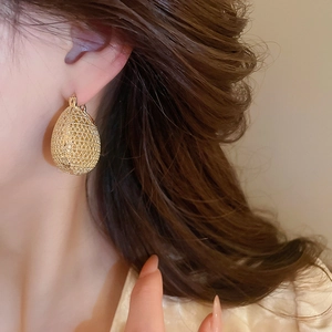 Close-up of golden teardrop earrings with woven texture worn by a female model