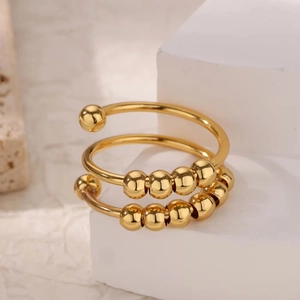 Detail of 18k gold spiral fidget ring with moving beads on a white geometric stand