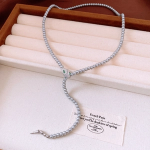 Macro detail of grey pearl necklace with snake head clasp and green gemstone eyes