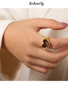 Détail d'une bague coeur dorée avec perles noires et design ajouré sur le doigt