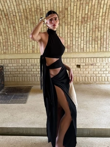 Elegant black backless halter maxi dress with high split detail against a brick background