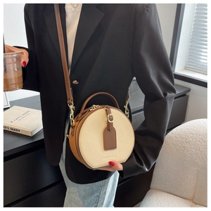 Detail of round beige and brown crossbody bag featuring fashion leather logo and adjustable strap