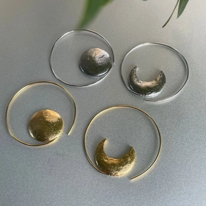 Detail of sun and moon asymmetric metal hoop earrings with hammered texture and finish