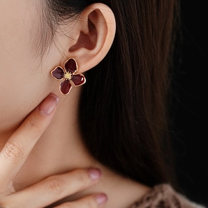 Macro detail of model wearing vintage deep red enamel flower earrings with gold borders