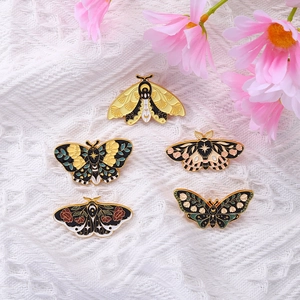 Set of five colorful moth enamel pins with floral and celestial patterns on lace background