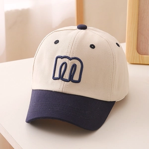 Detail shot of navy blue embroidered letter M on cream cotton baseball cap for kids