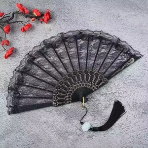 Detail view of a black lace folding fan with intricate hollow patterns and black tassel